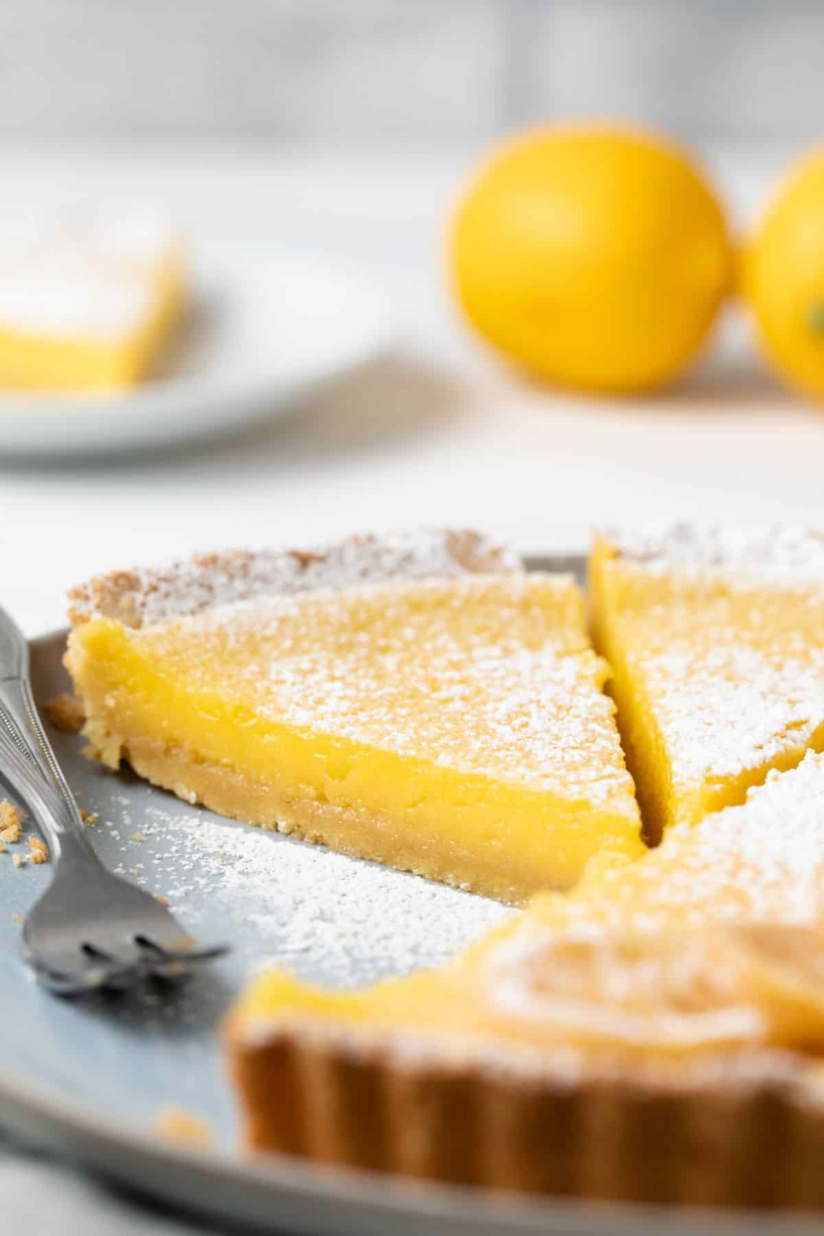 Side view of slice of lemon tart on a plate with fork.