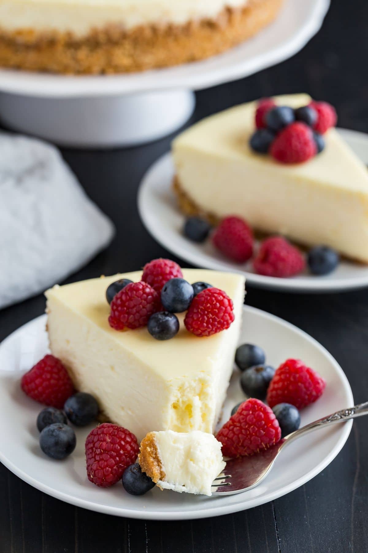 A slice of cheesecake topped with fresh berries and a fork taking out a bite.