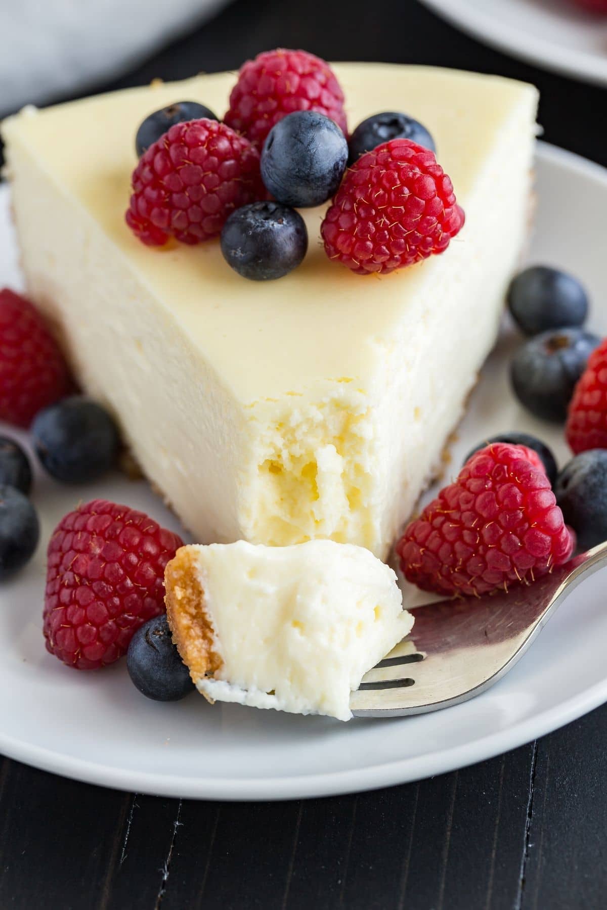 The best cheesecake slice on a plate with a fork taking out a bite.