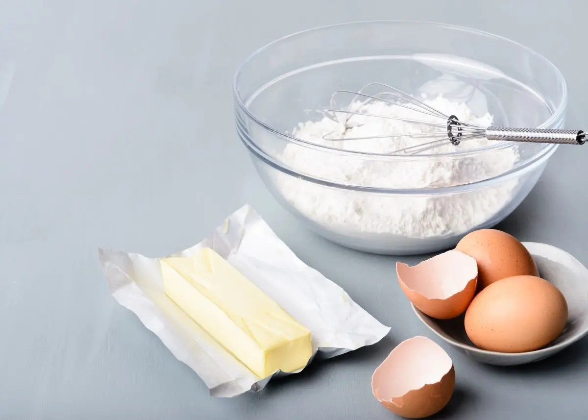 butter, eggs, and bowl of flour with whisk