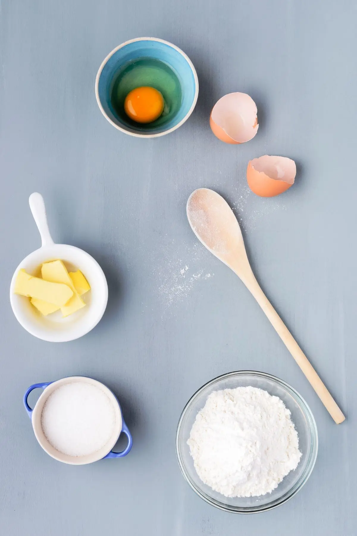 wooden spoon with bowl of eggs, bowl of butter, bowl of sugar, and bowl of flour