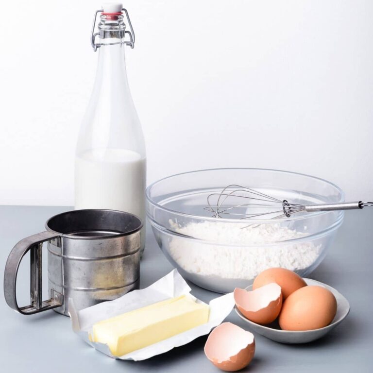 eggs, butter, flour in glass bowl, jar of milk, and metal flour sifter