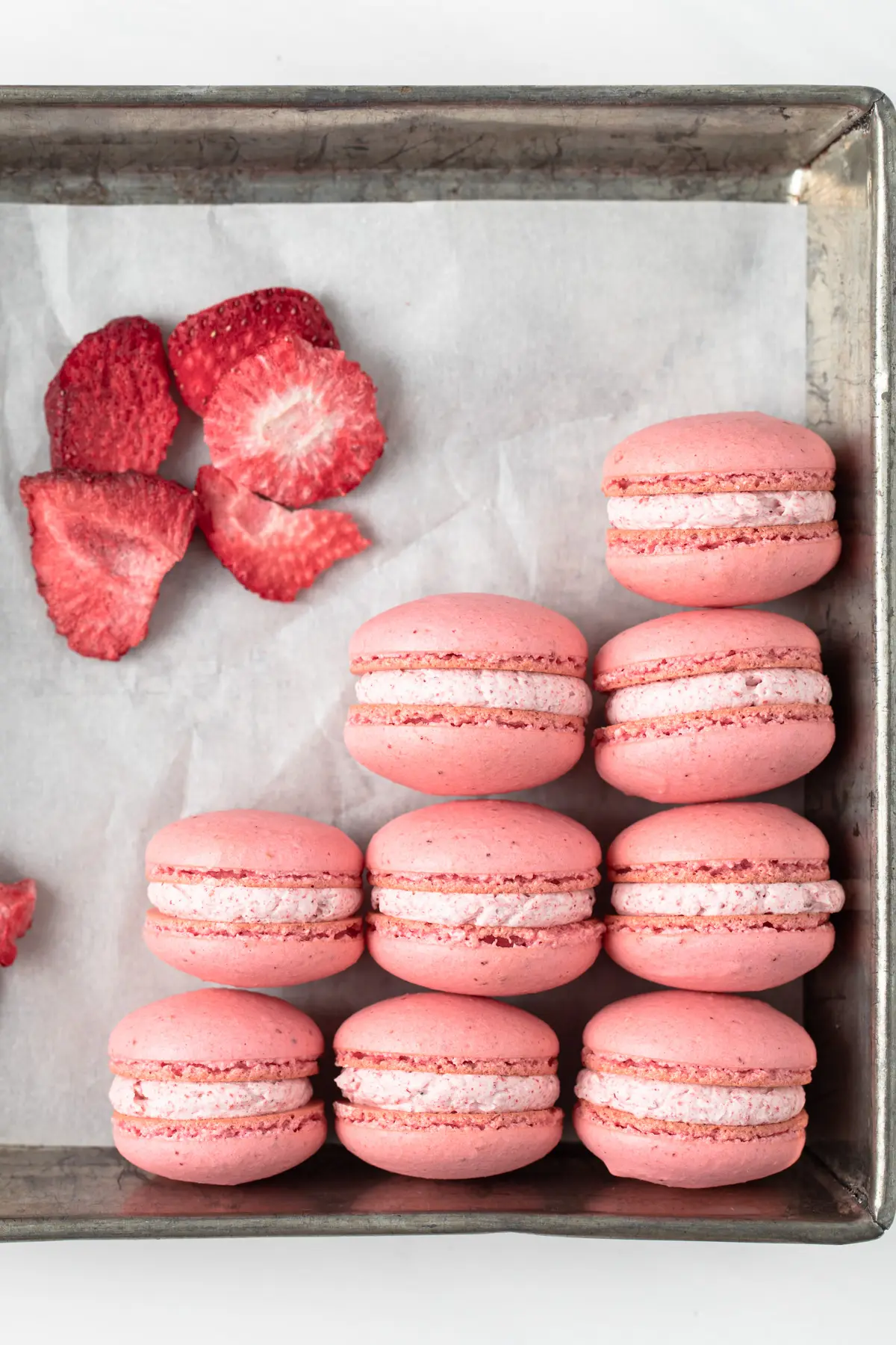 macarons with strawberry buttercream neatly arranged in a parchment lined baking pan