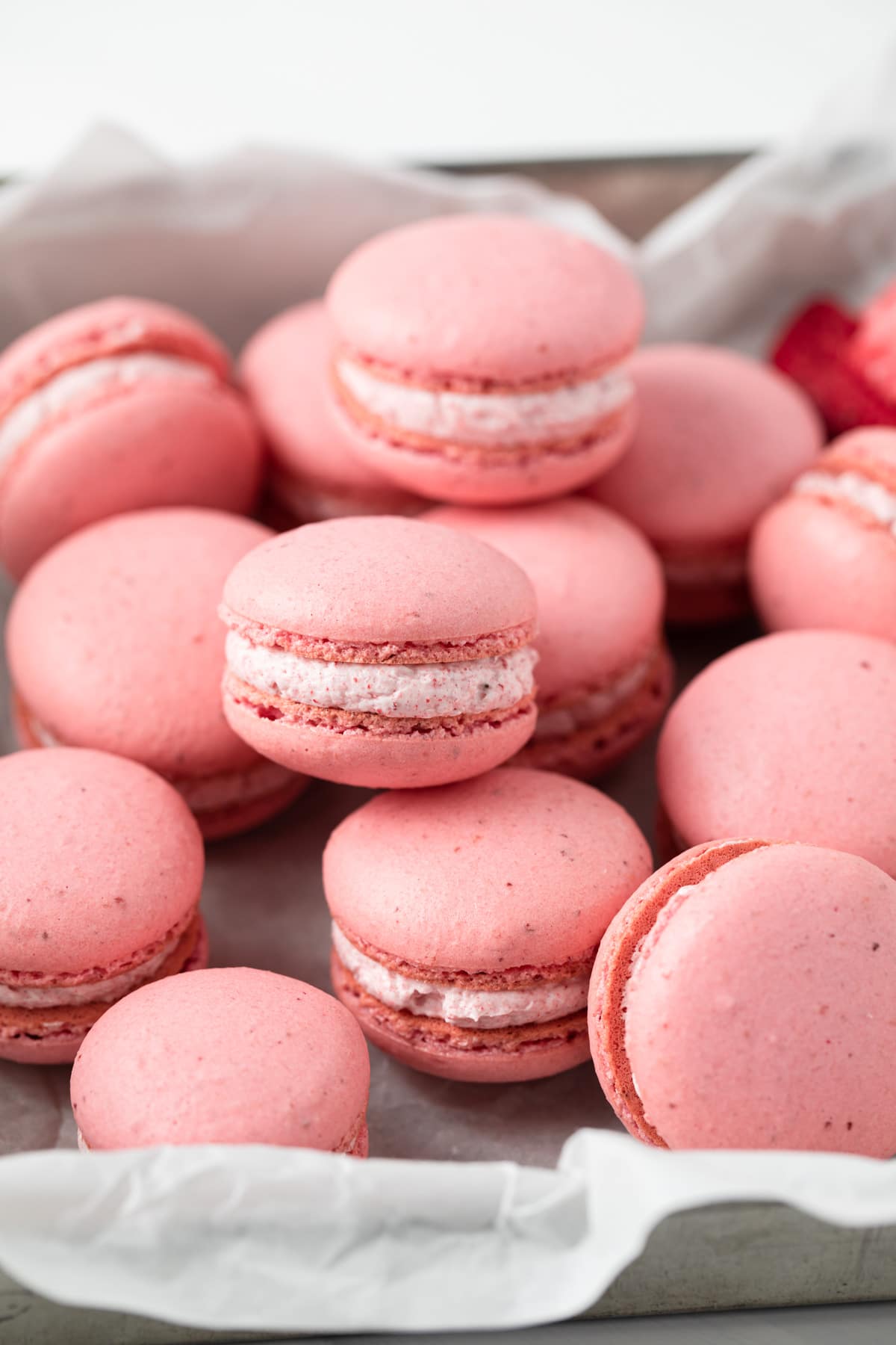 strawberry macarons scattered in a baking sheet liked with parchment paper