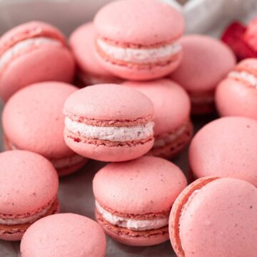strawberry macarons scattered in a baking sheet liked with parchment paper