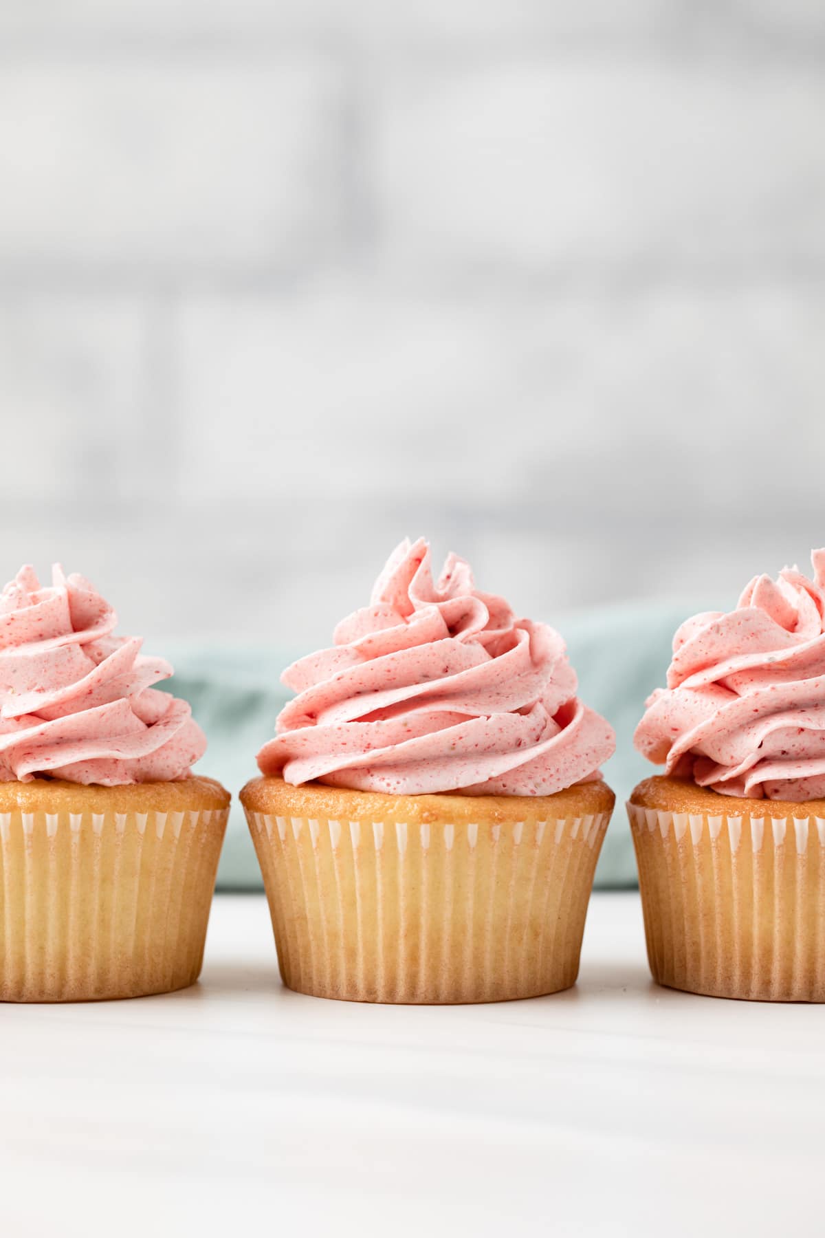 strawberry frosting swirled on three vanilla cupcakes
