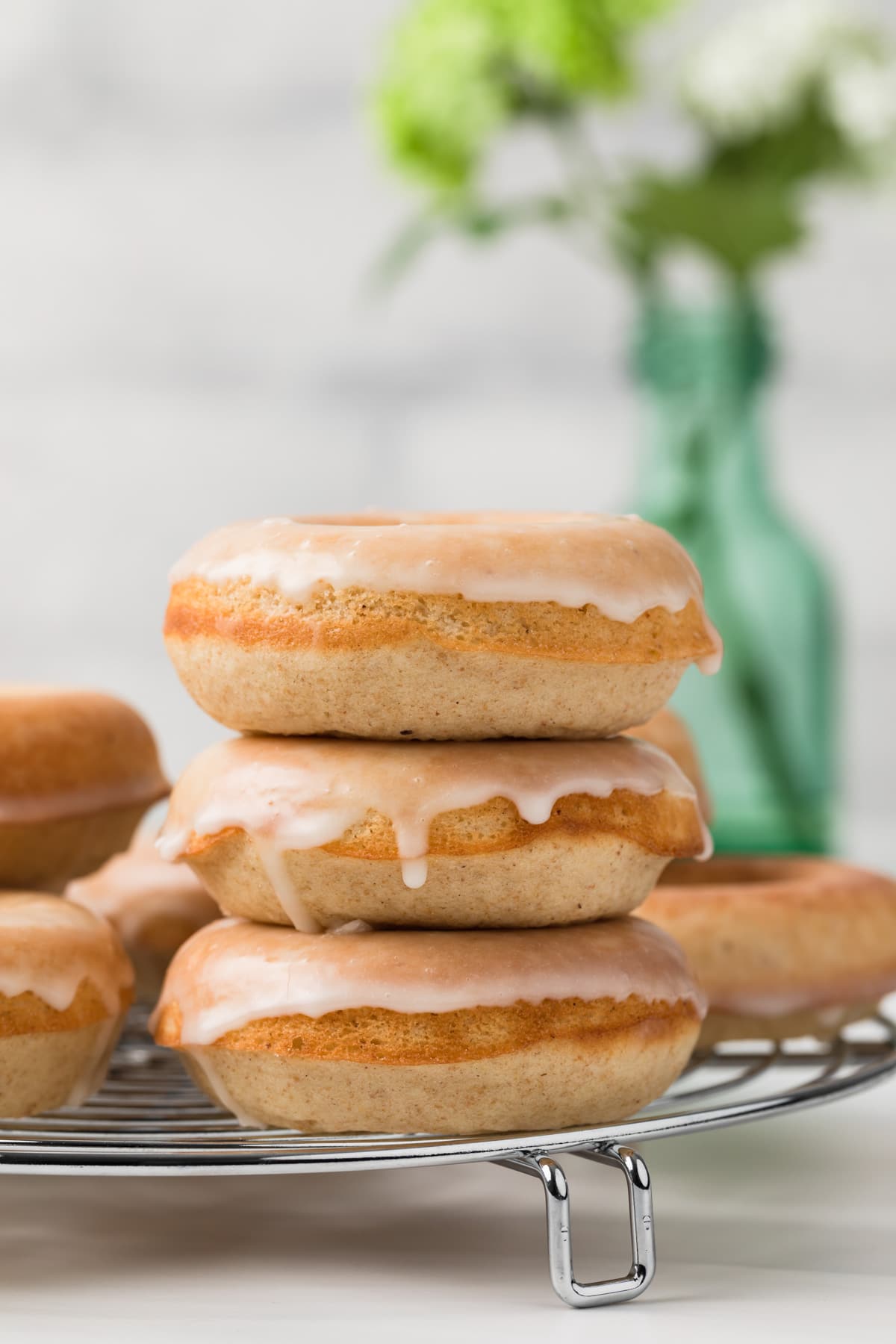 baked donuts stacked three high on round metal rack with glass flower vase in background