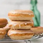 baked donuts stacked three high on round metal rack with glass flower vase in background