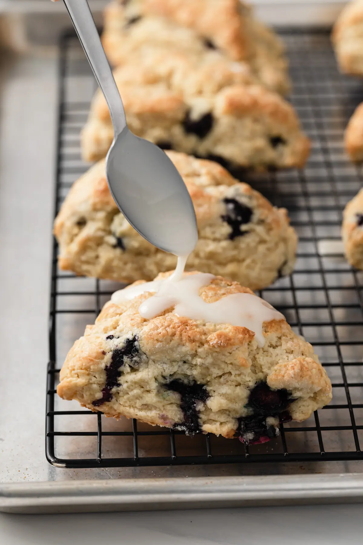 glaze being spooned over blueberry scones on a black wire rack