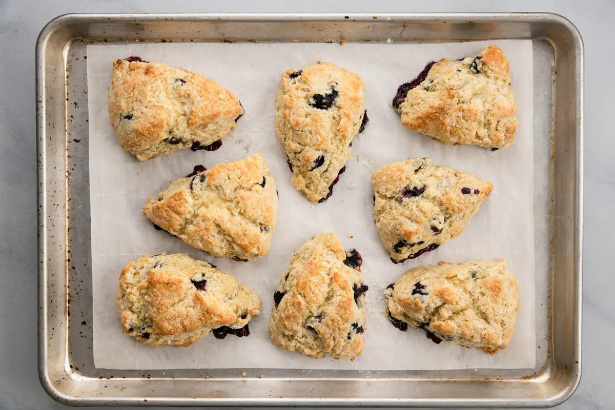 overhead of baked blueberry scones on baking sheet lined with white parchment paper