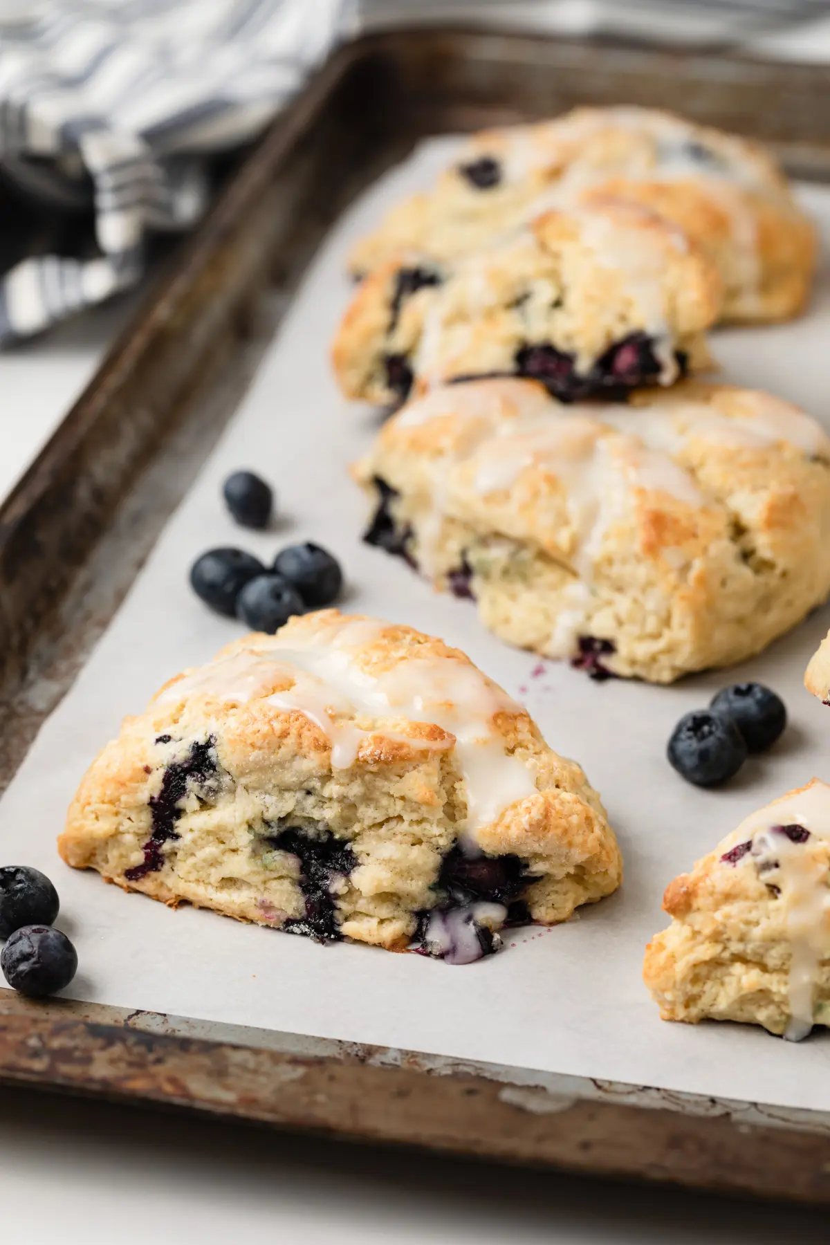 angled view of blueberry scones and fresh blueberries on a baking sheet lined with white parchment paper