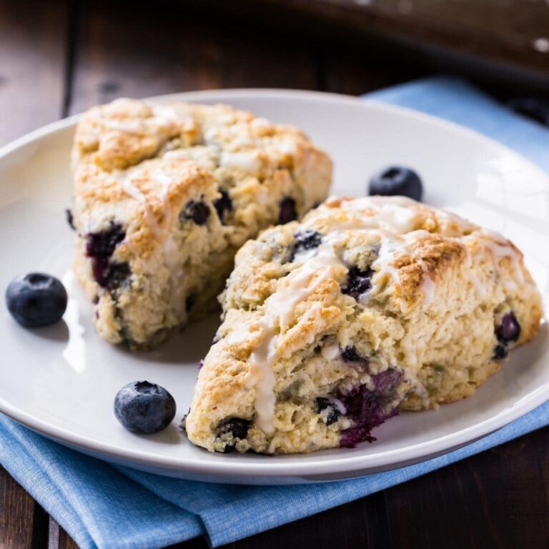Two blueberry scones on a white plate with a baking sheet in the background.