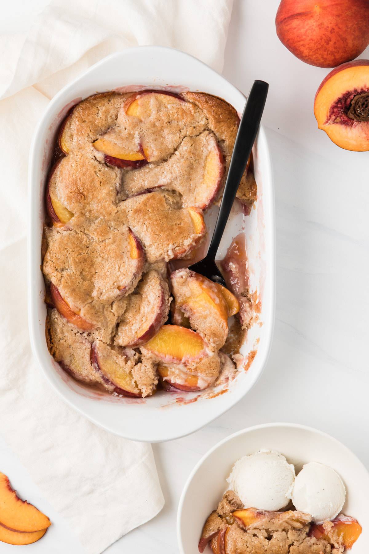 overhead view of peach cobbler in white casserole with black spoon