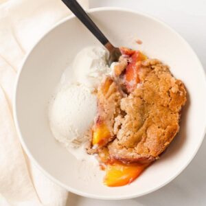 closeup of peach cobbler with vanilla ice cream in white bowl