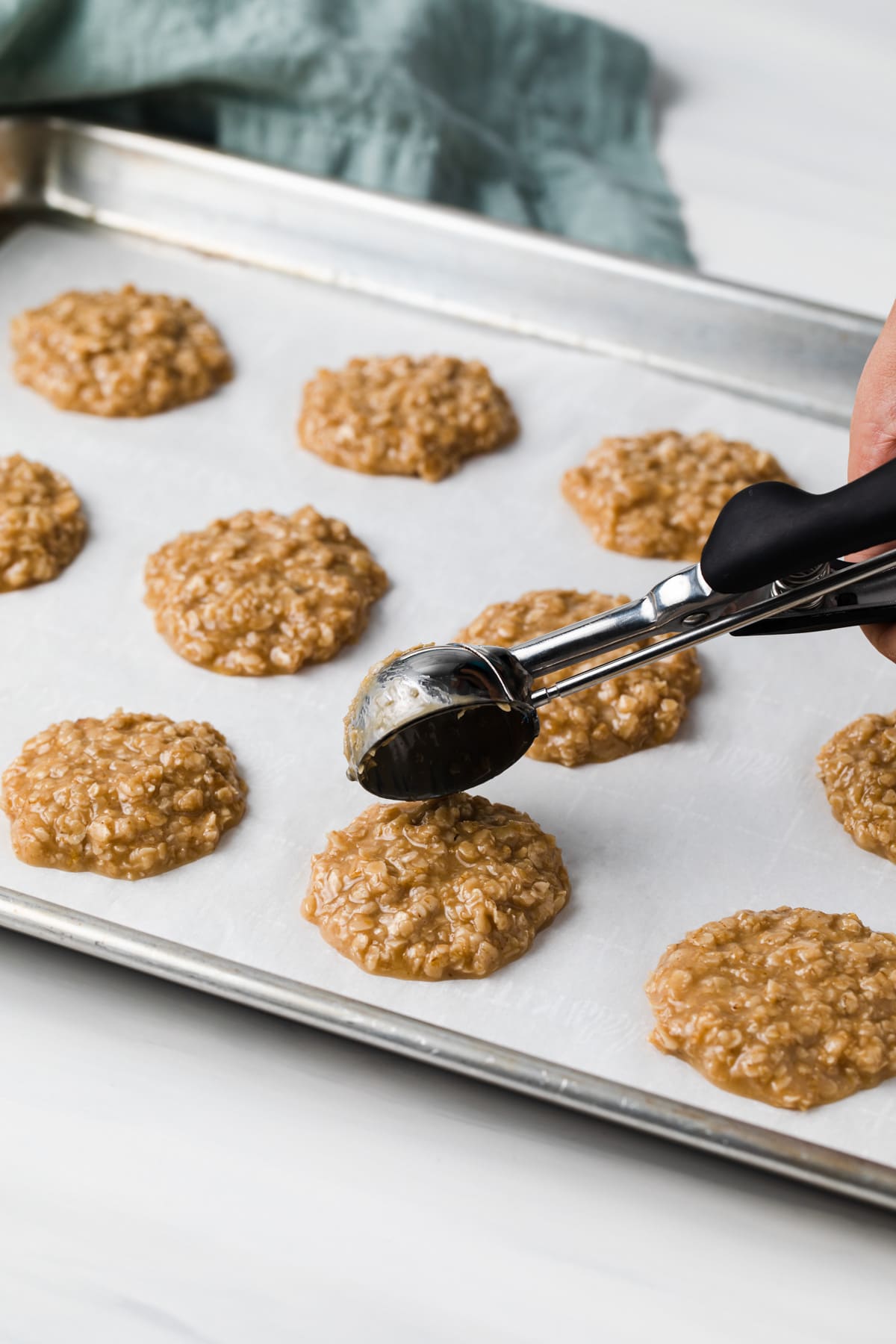 scoop dropping peanut butter no bake cookies onto a baking sheet lined with white parchment paper