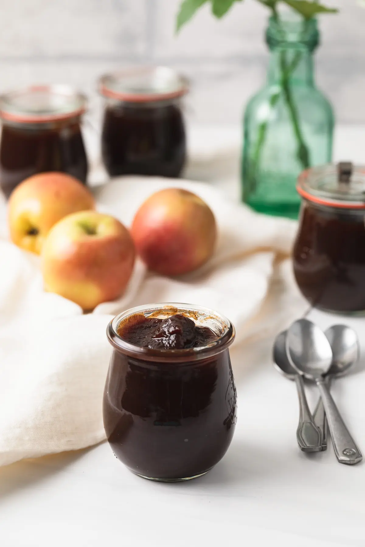 jars of apple butter with three apples and spoons nearby