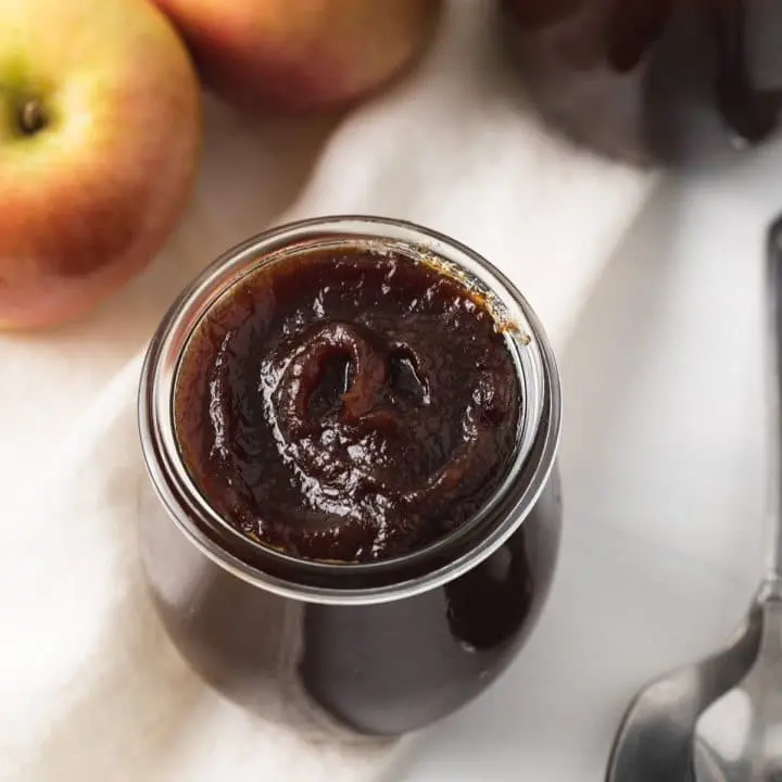 high angled view of apple butter in glass jar with apple and jar of apple butter behind it