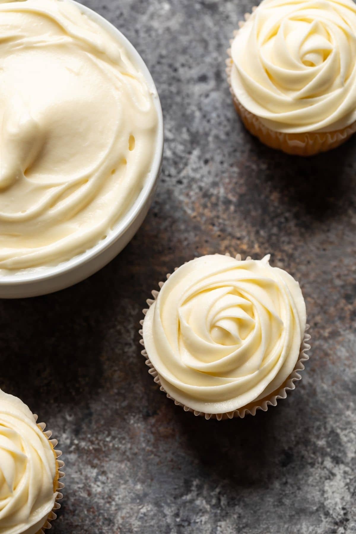 Overhead view of cream cheese frosting swirled over yellow cupcakes