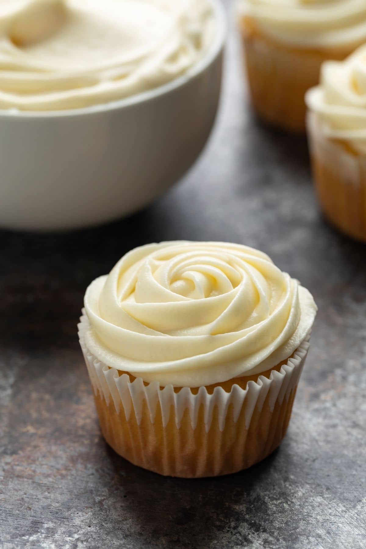 Side view of cream cheese frosting swirled over yellow cupcakes