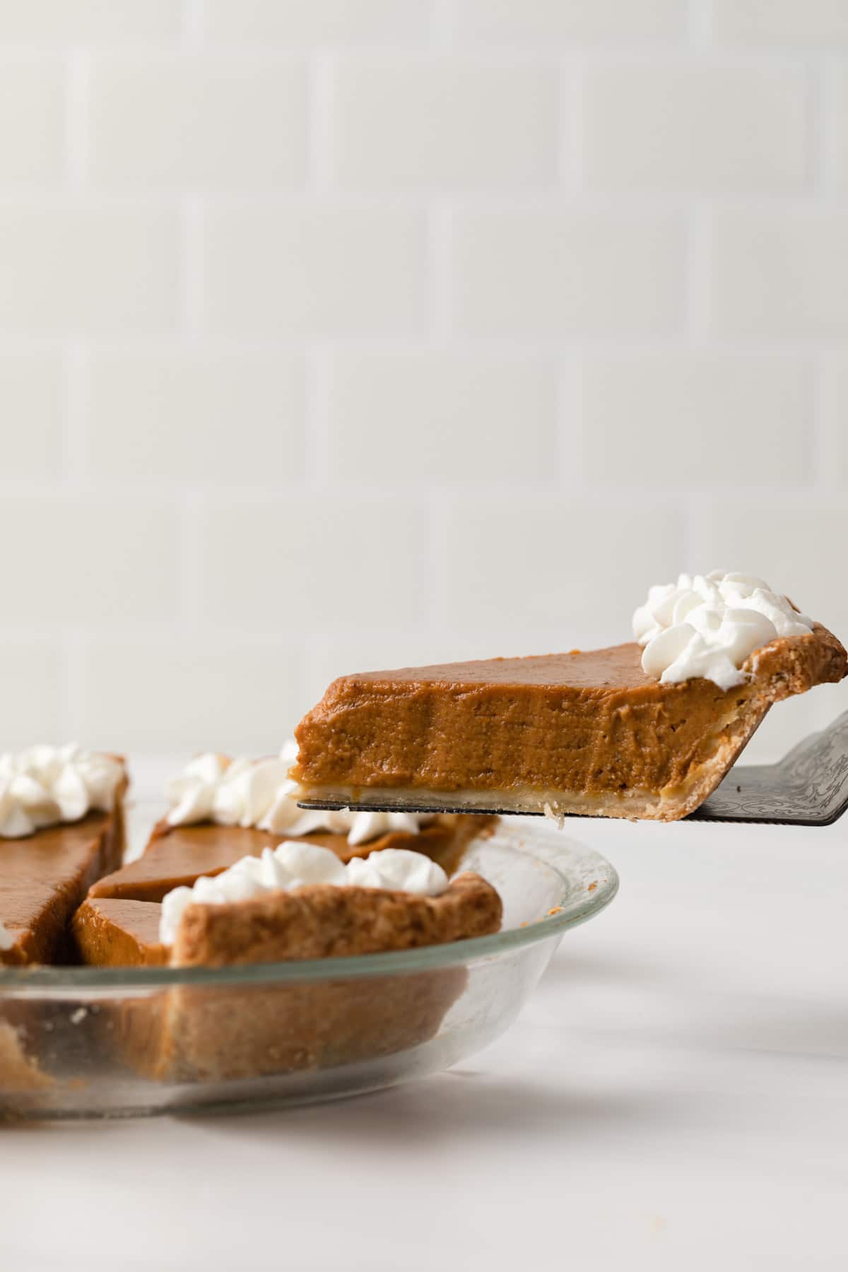 slice of pumpkin pie being taken out of pie in glass dish