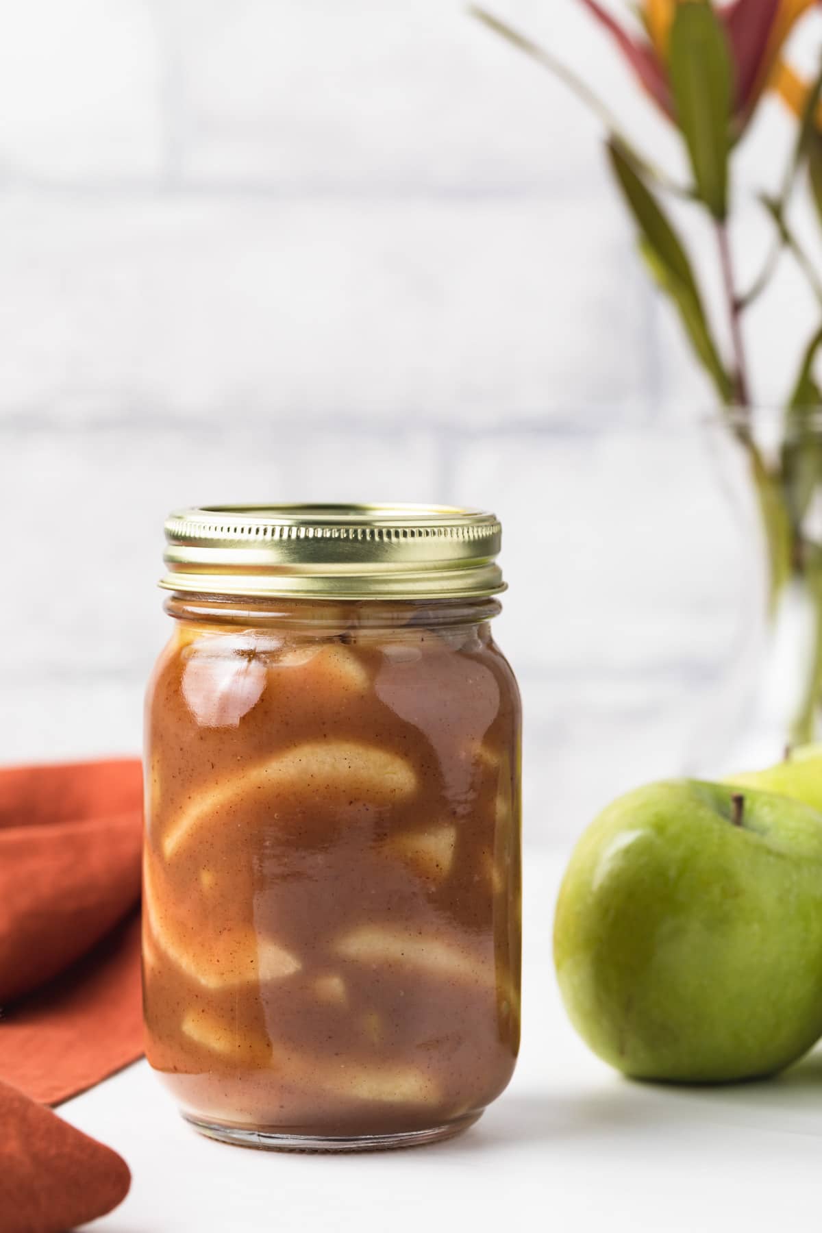 apple pie filling in glass jar next to green apples and orange napkin