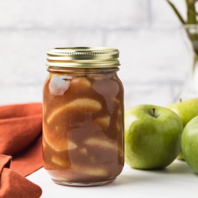 apple pie filling in glass jar next to green apples and orange napkin