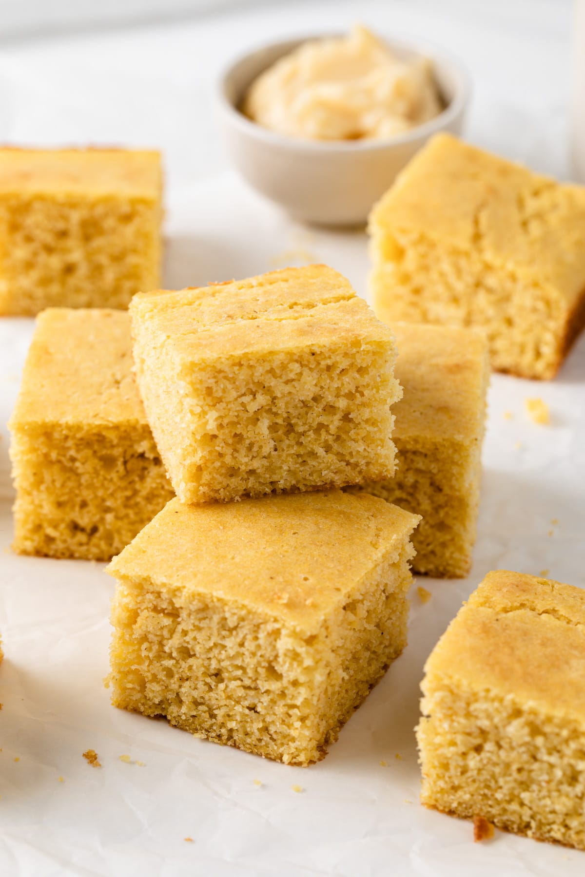 southern cornbread squares stacked on a white background with bowl of butter behind