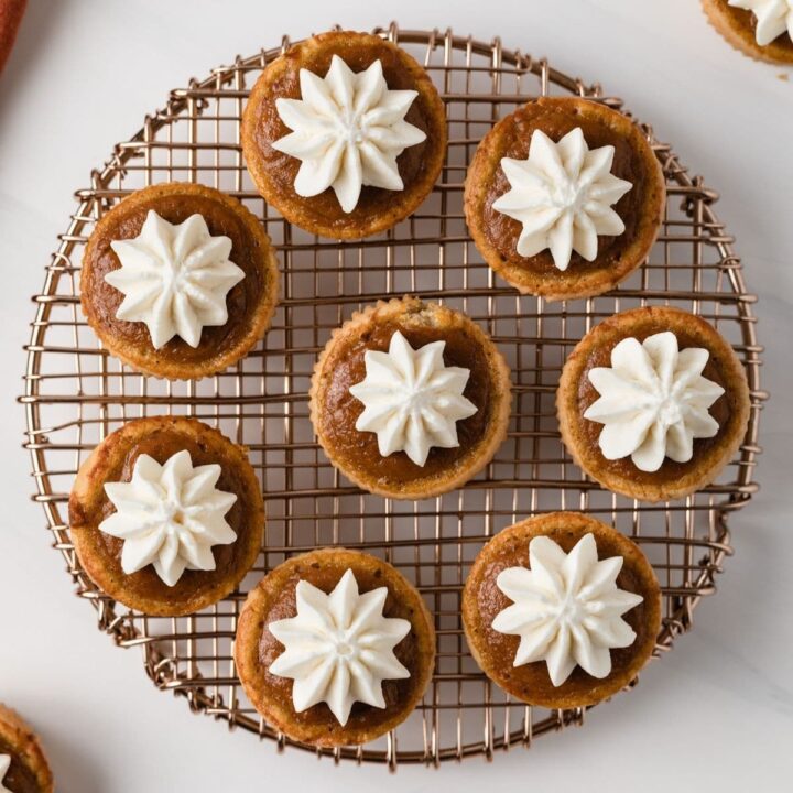 overhead of mini pumpkin pies with whipped cream set on a round wire rack