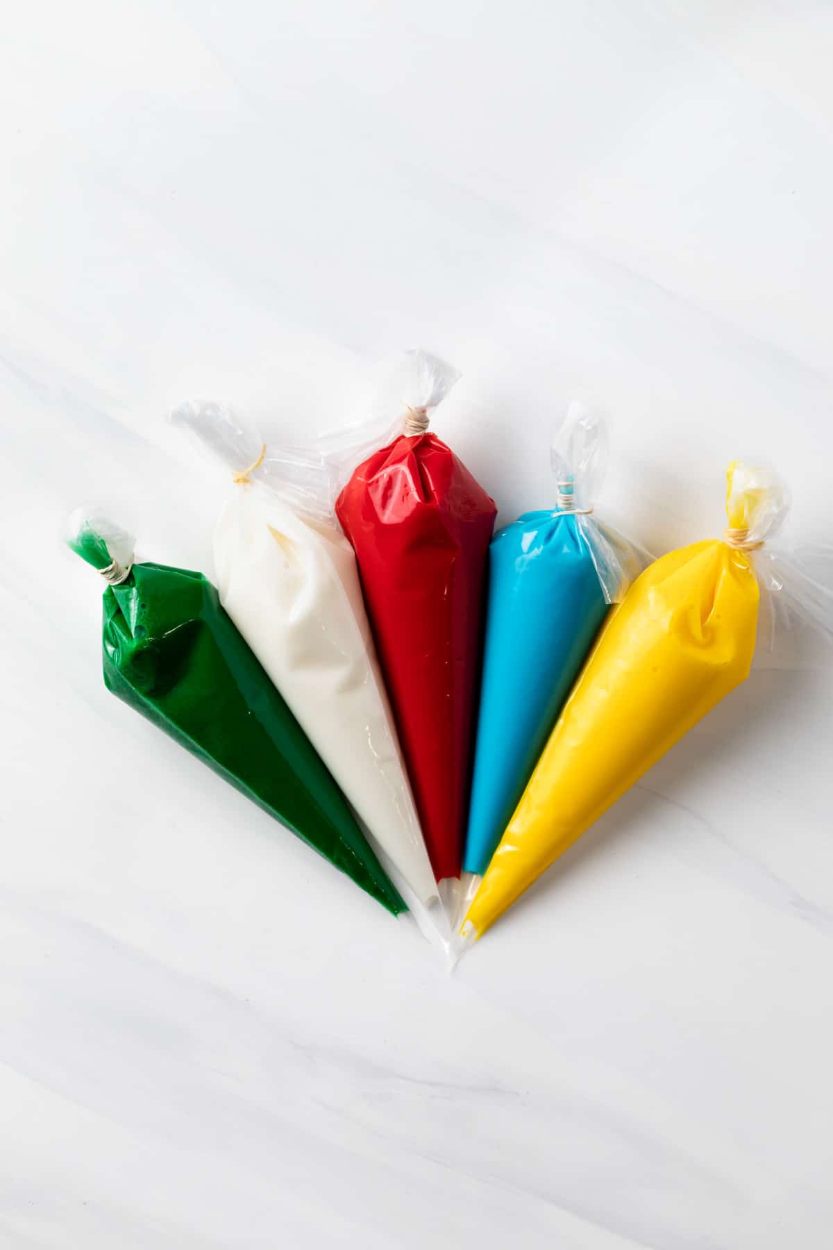 green, white, red, blue, and yellow sugar cookie icing in piping bags