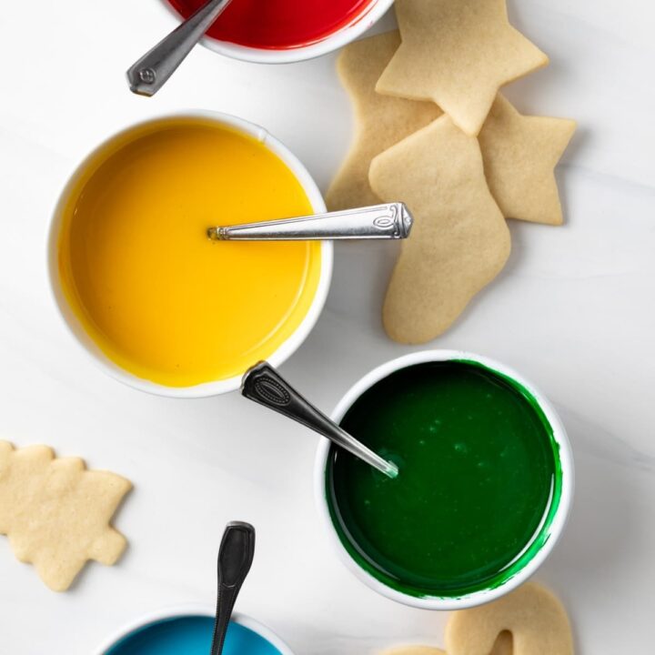 bowls of red, yellow, green, and blue icing with sugar cookies