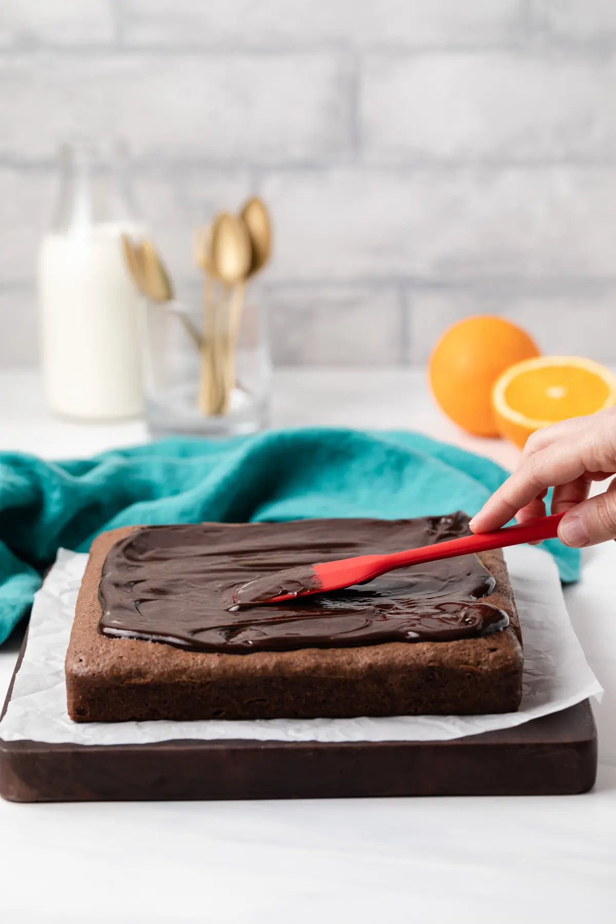 chocolate ganache being spread over chocolate orange brownies with red spatula