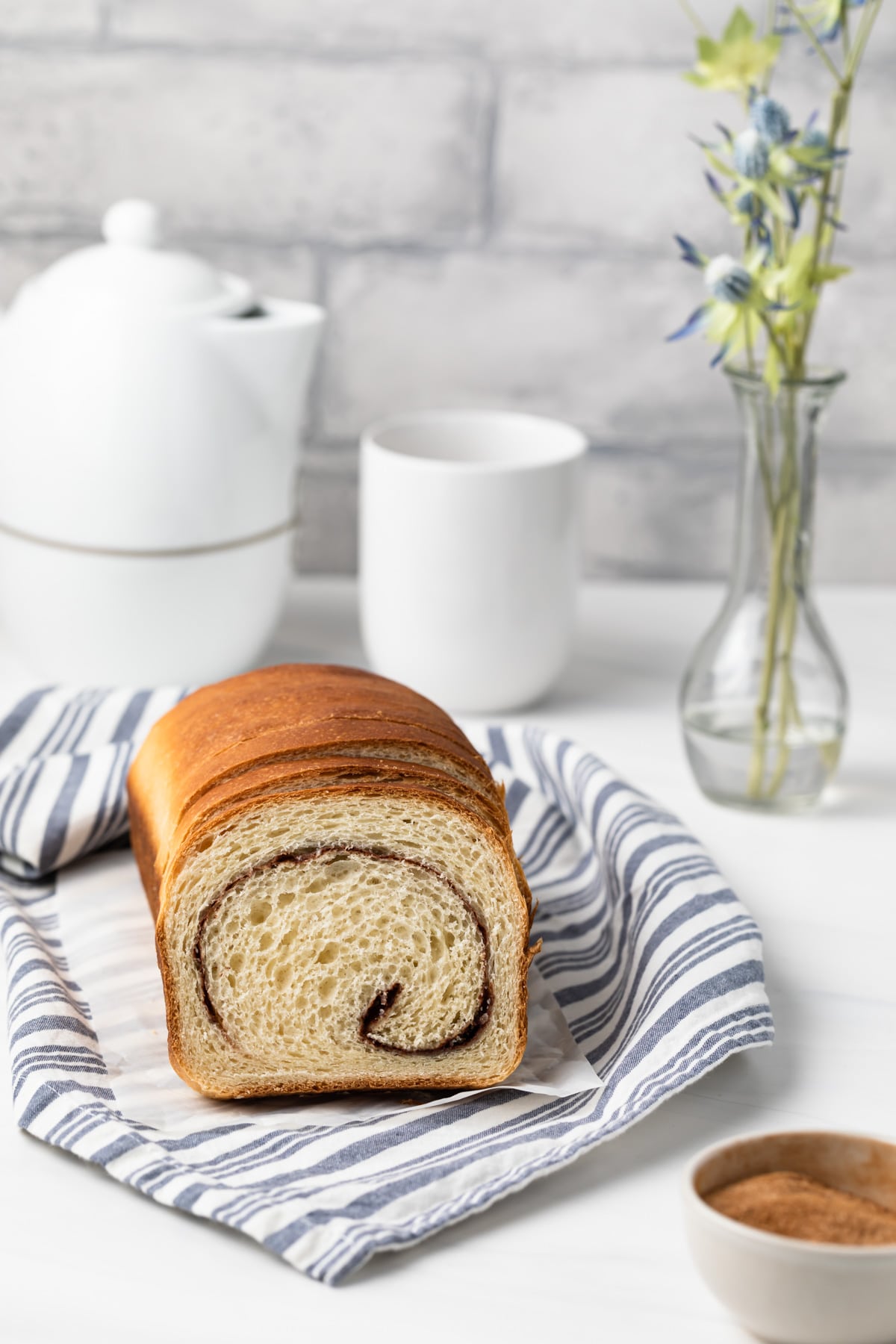 bread with cinnamon swirl on blue striped tea towel with tea pot and cup