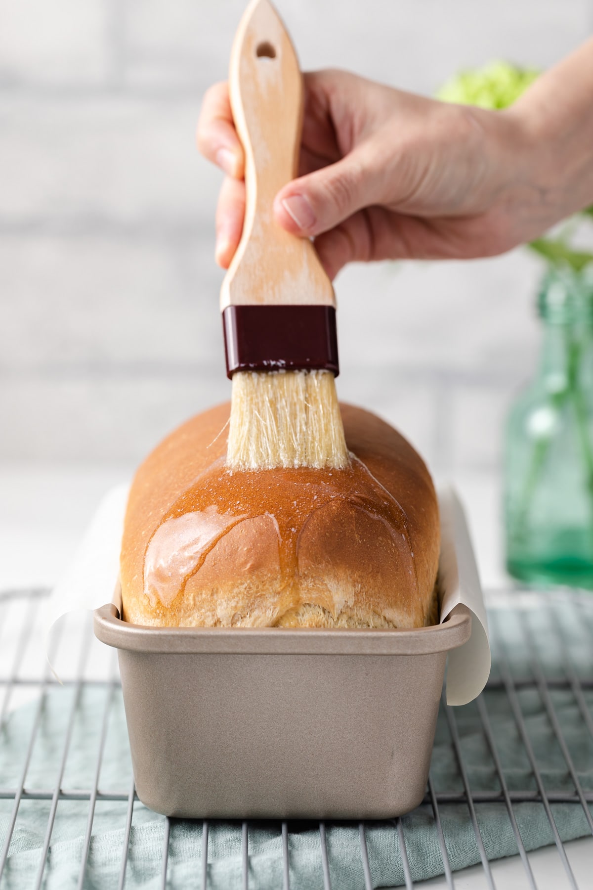 brushing butter over baked bread in loaf pan with pastry brush