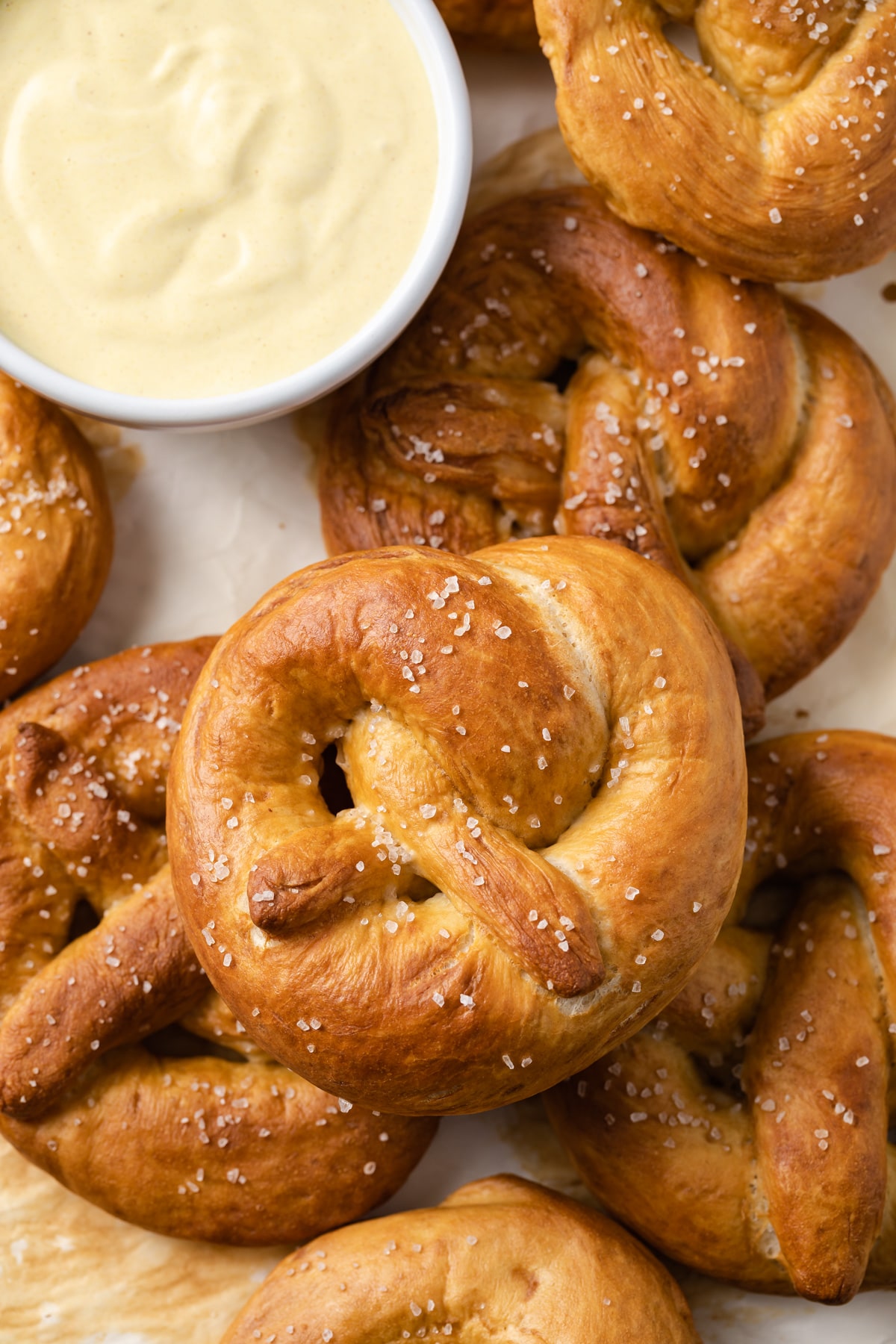 overhead close up of soft pretzels on a baking sheet with white bowl of mustard sauce