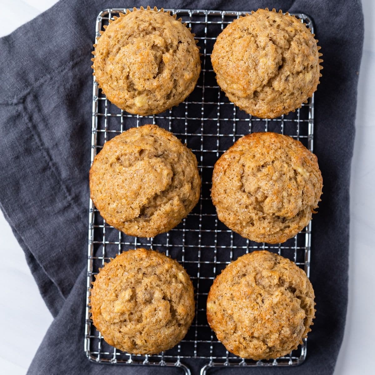 overhead of six banana muffins on a wire rack with blue napkin underneath