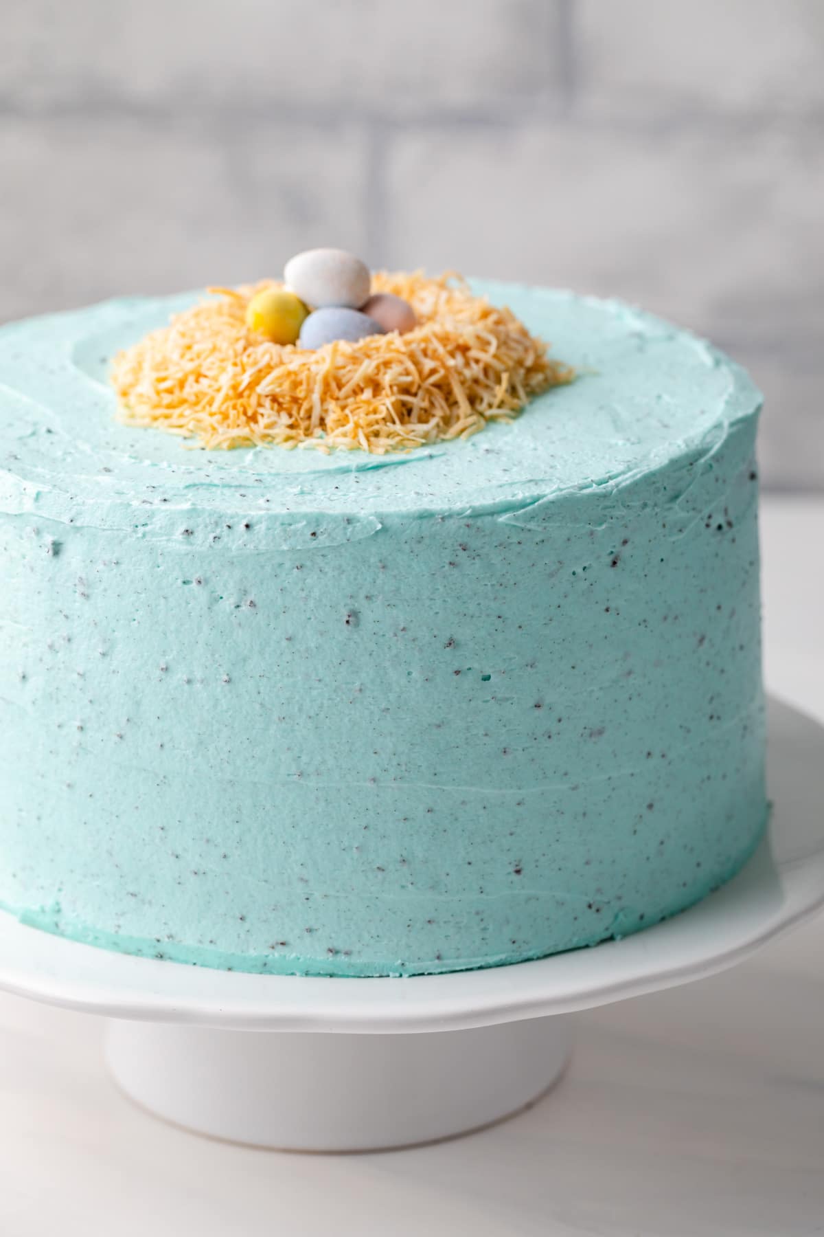 cake with blue frosting, coconut birds nest, and candy robin eggs on a white cake stand