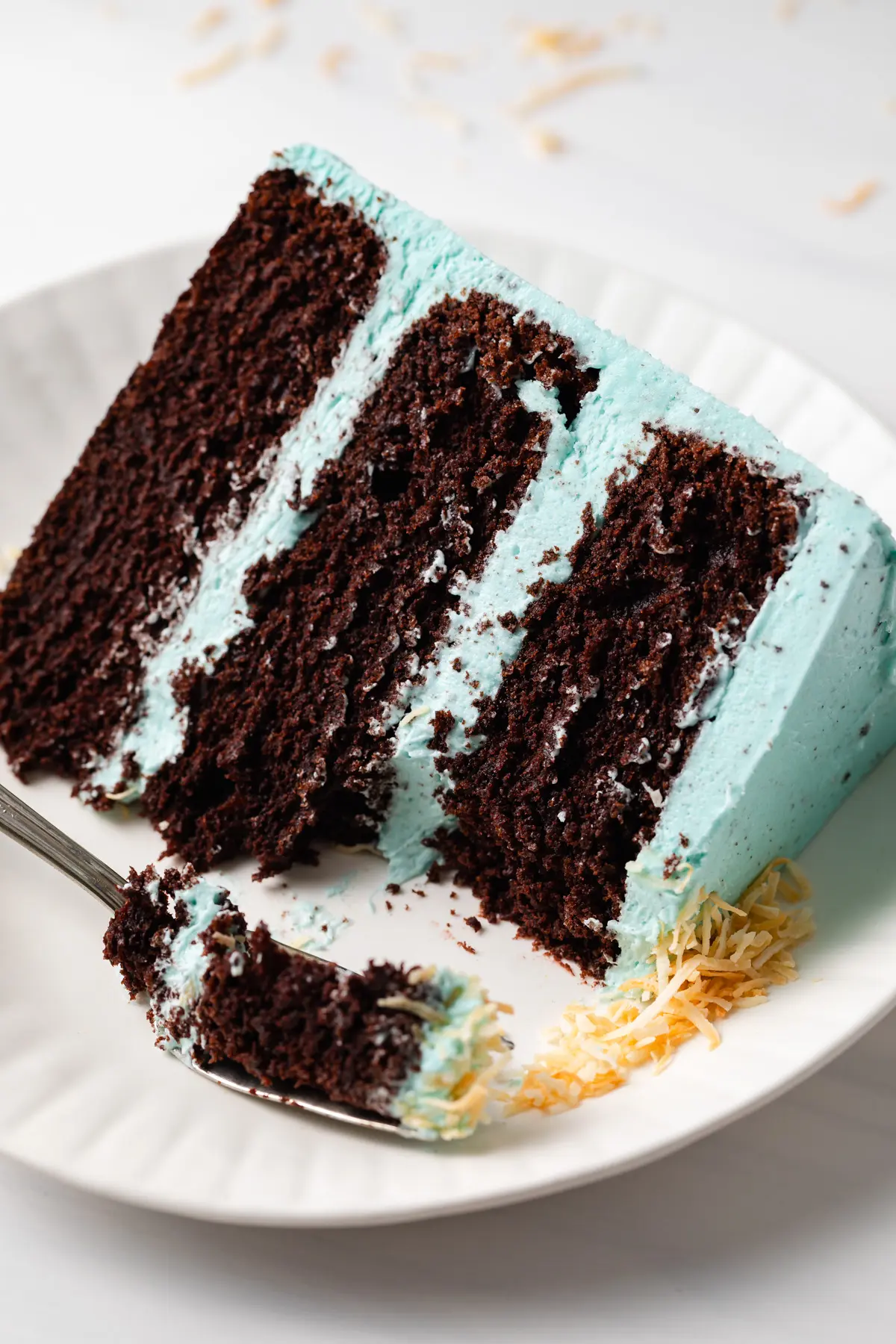 fork taking a bite out of a slice of chocolate cake with blue icing on white plate