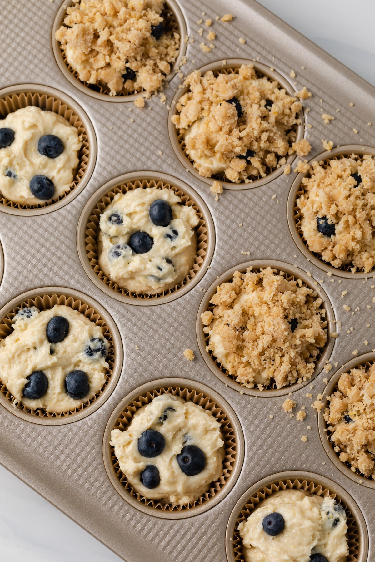 overhead of muffin batter in muffin pan with a streusel topping over half the muffins