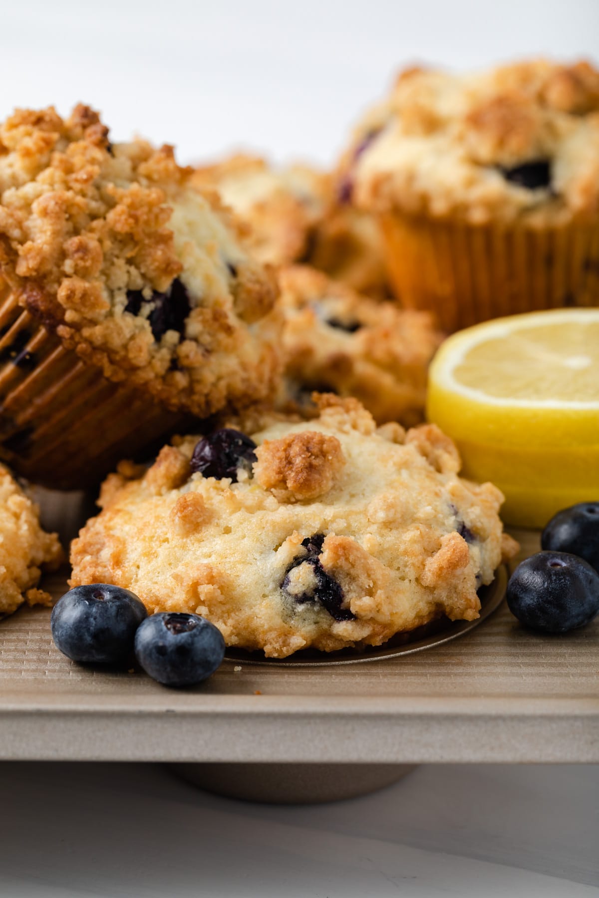 side view of lemon blueberry muffins in a muffin pan with a couple muffins sitting on top of the pan