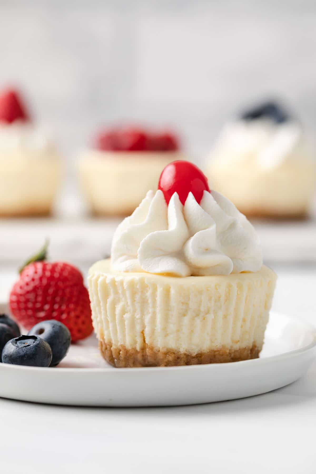 mini cheesecake topped with whipped cream and a cherry on a white plate