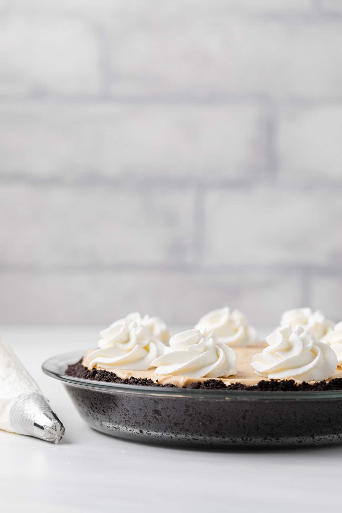 side view of no bake peanut butter pie in glass pie pan and whipped cream swirls on top