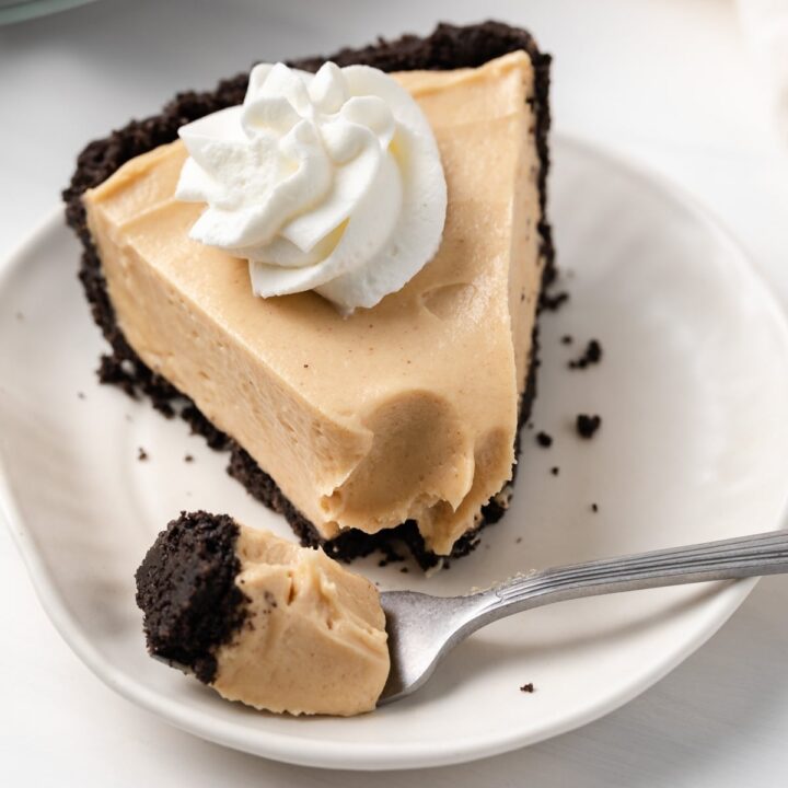 angled view of creamy peanut butter pie topped with whipped cream on a white plate with fork taking a bite out