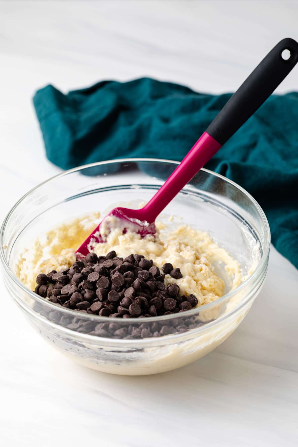 chocolate chips added to muffin batter in glass bowl with pink spatula