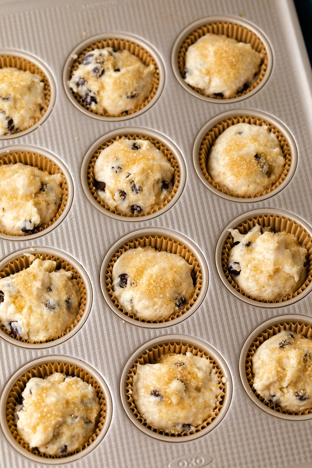 chocolate chip muffin batter topped with coarse sugar in muffin pan lined with paper liners