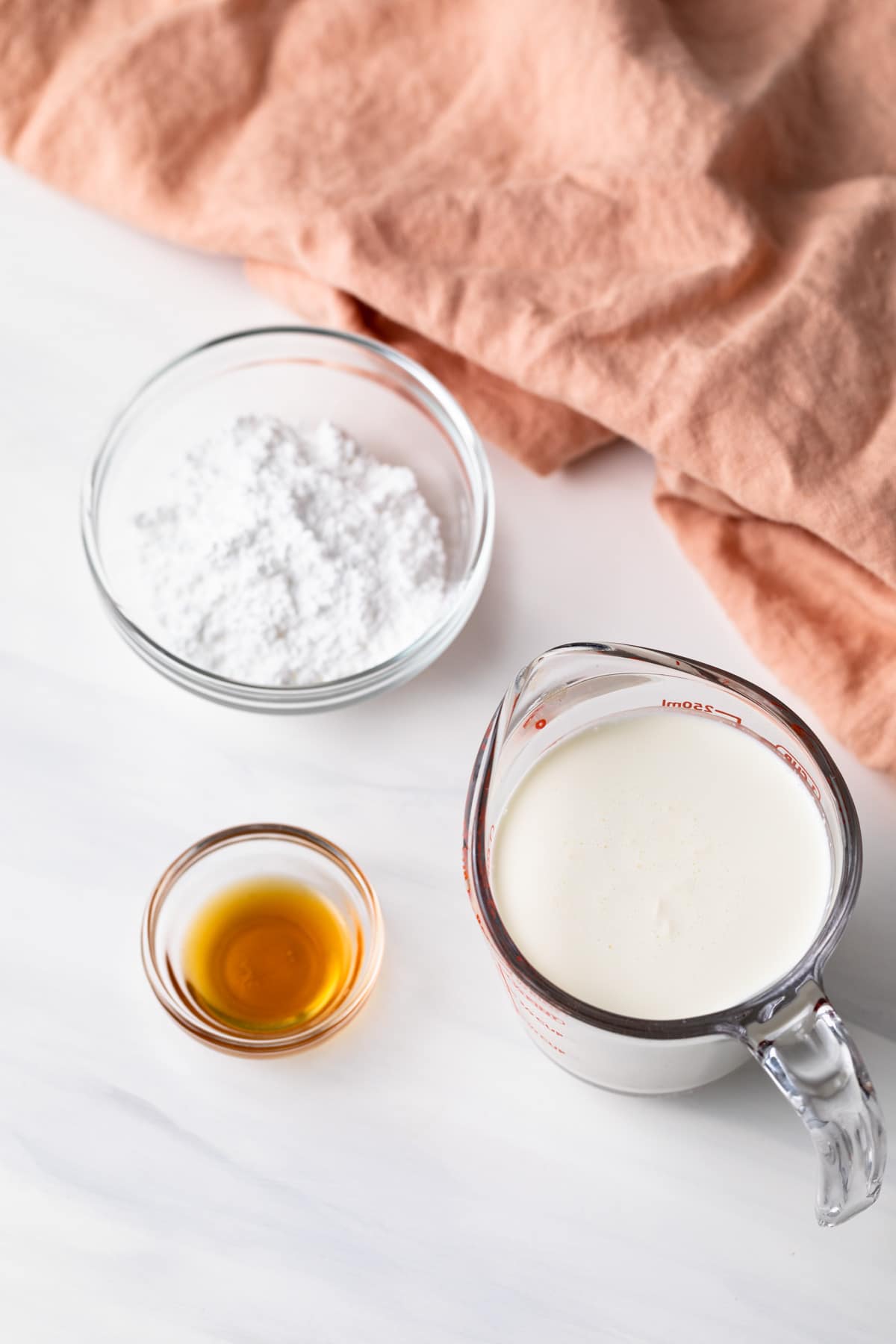 bowl of powdered sugar, bowl of vanilla extract, and glass measuring cup with heavy cream