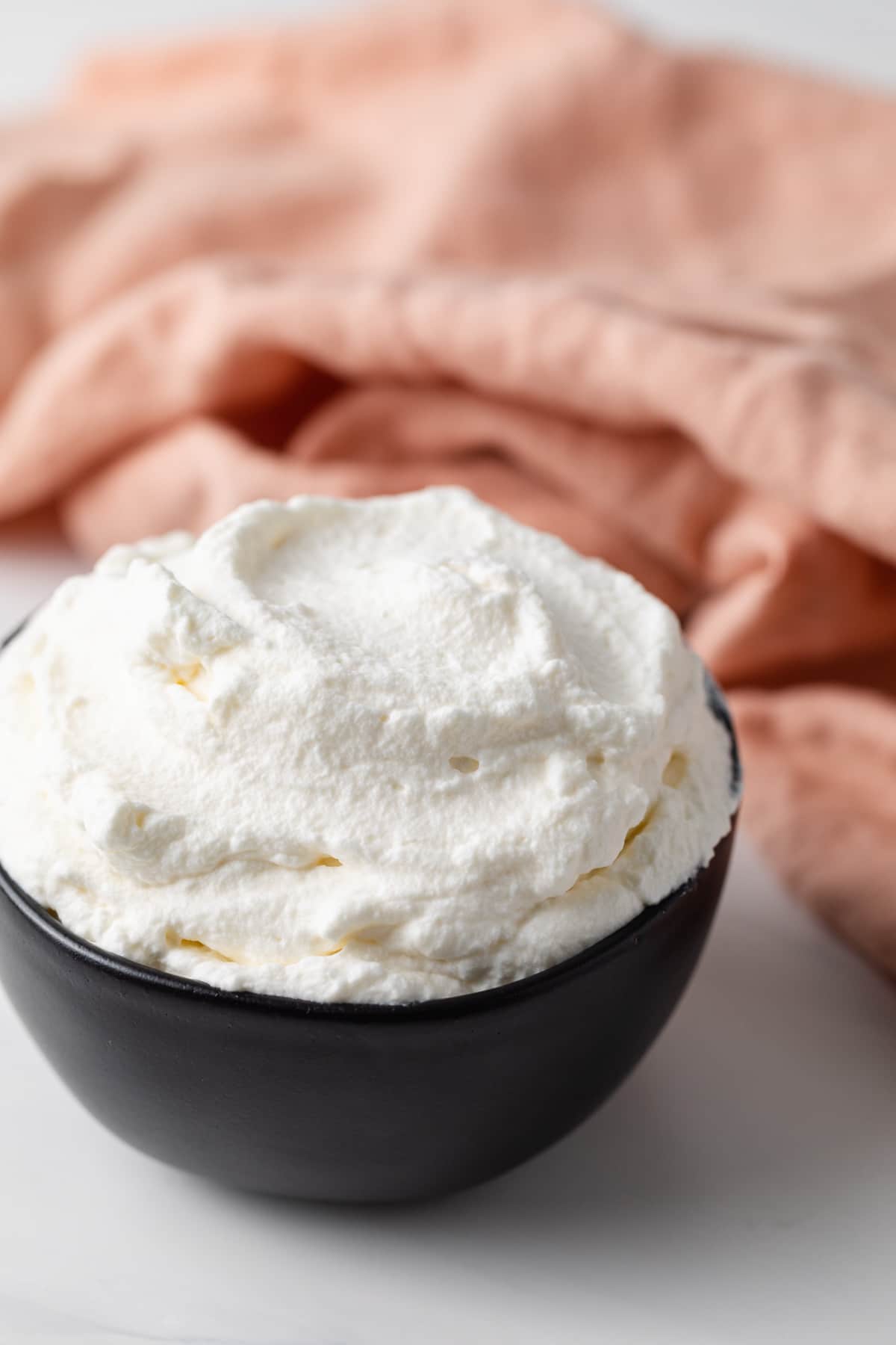 whipped cream in black bowl with peach colored napkin in background