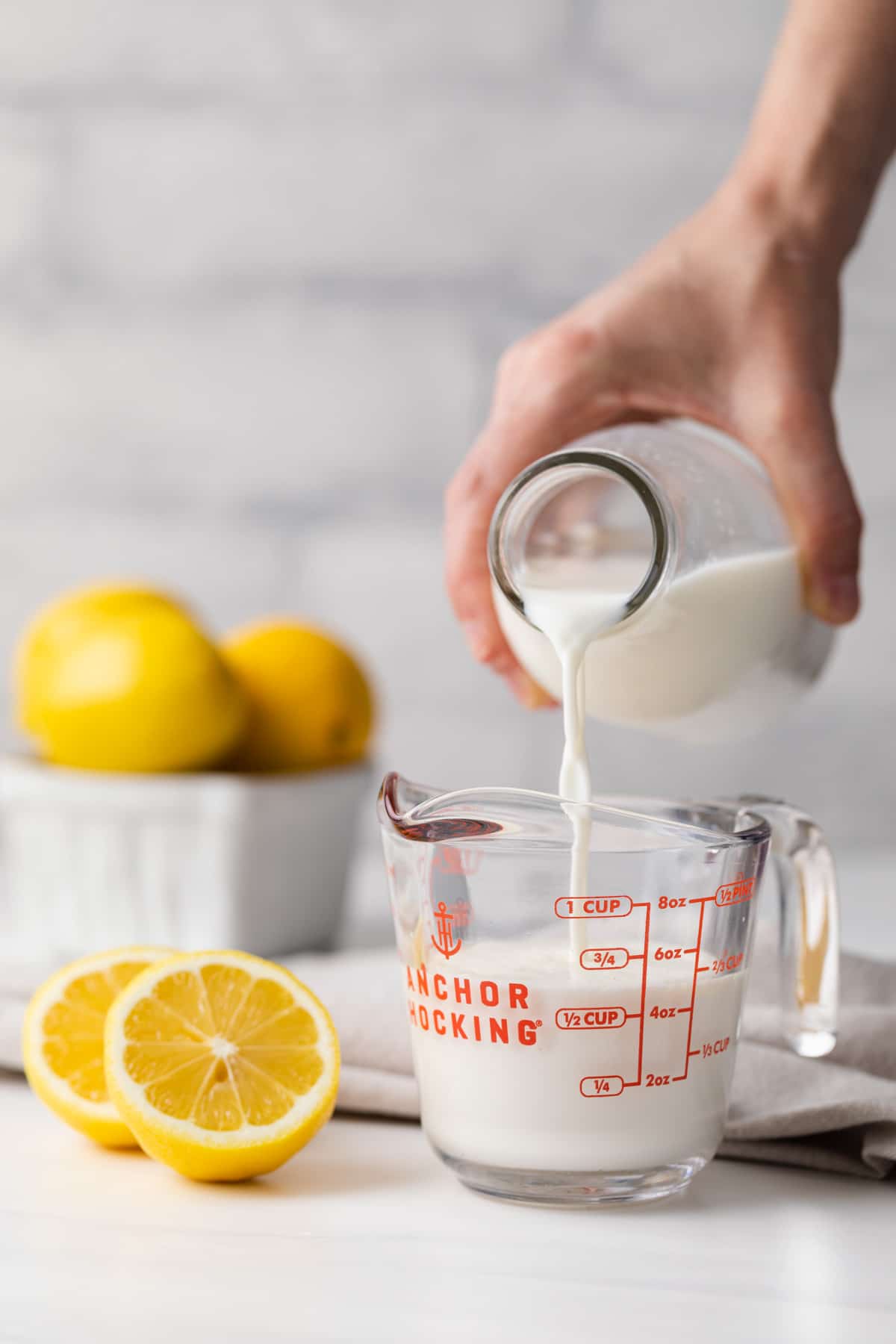 a glass measuring cup being filling with milk along with lemons and napkin in background