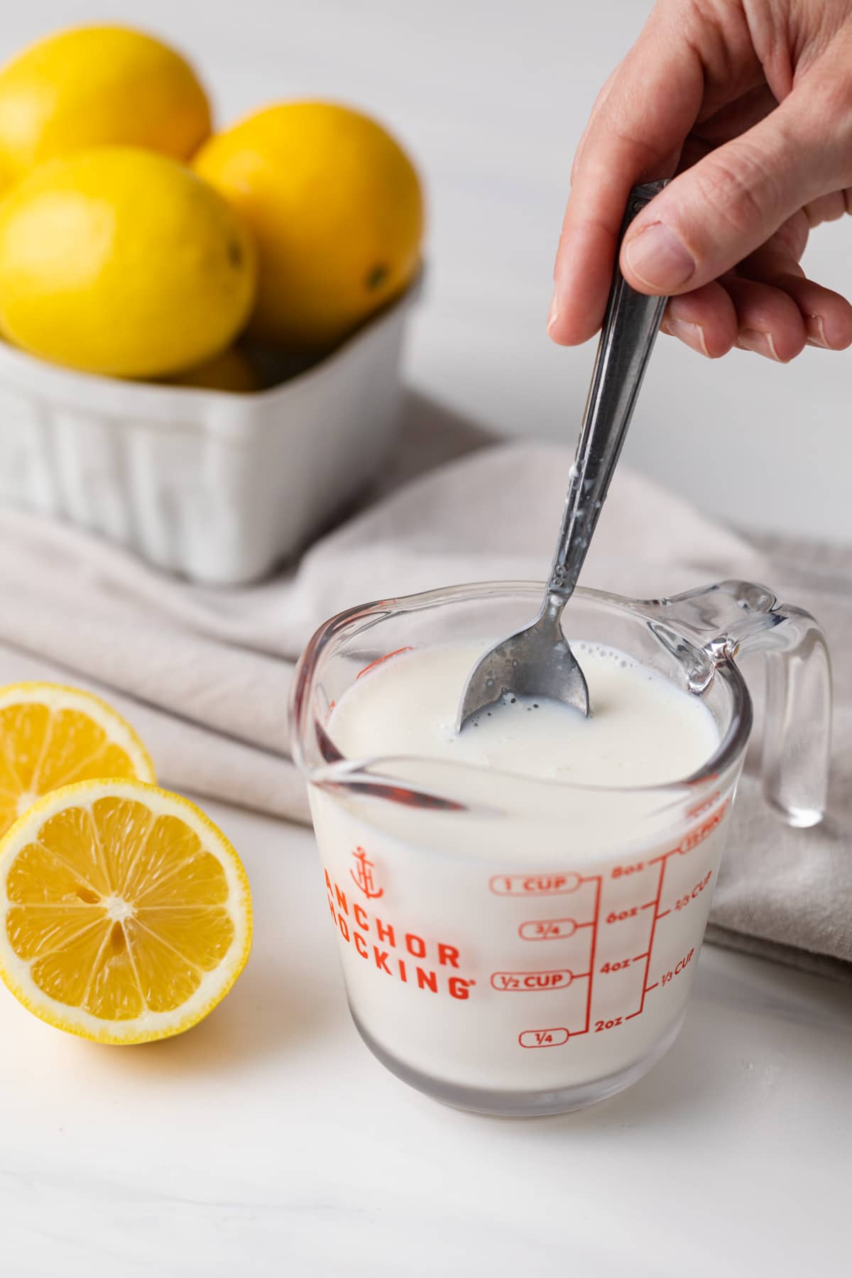 spoon stirring buttermilk substitute in glass measuring cup with lemons and napkin in background