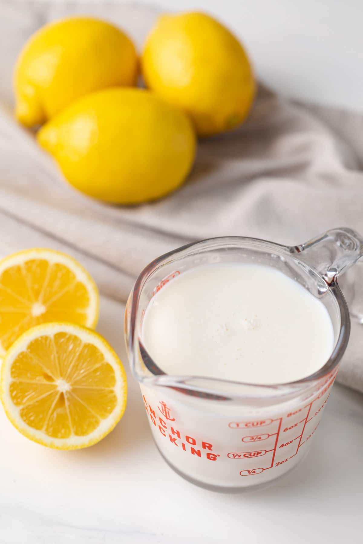 glass measuring cup filled with homemade buttermilk along with lemons and napkin in background