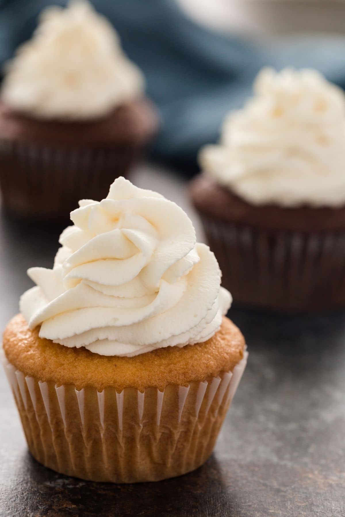 whipped cream swirled over a vanilla cupcake with chocolate cupcakes in the background